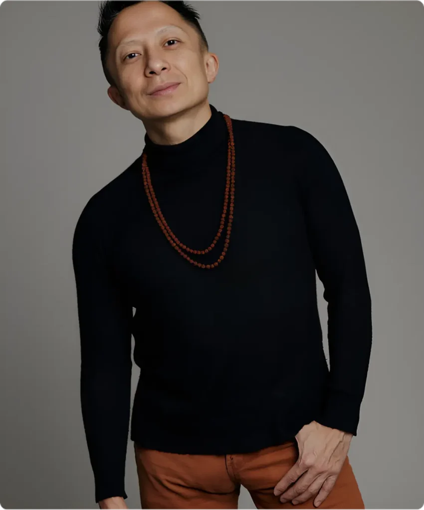 Professional portrait of Kwok One in a dark pinstripe suit against a grey background – corporate headshot with confident expression and formal attire.