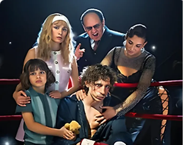 A weary boxer sits on a stool in a boxing ring, flanked by supportive family and friends, conveying a mix of determination and camaraderie. The word "BOXER" is overlaid.