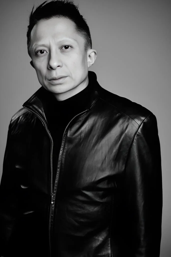 Professional portrait of Kwok One in a dark pinstripe suit against a grey background – corporate headshot with confident expression and formal attire.