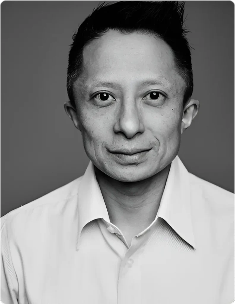 Professional portrait of Kwok One in a suit against a grey background – corporate headshot with confident expression and formal attire.